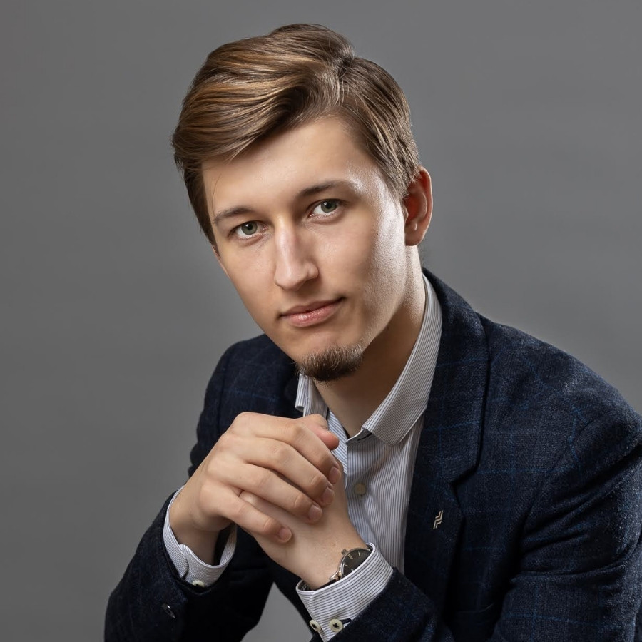 Bartosz Orzewski portret studyjny w garniturze, Bartosz siedzi ze splecionymi palcami dłoni